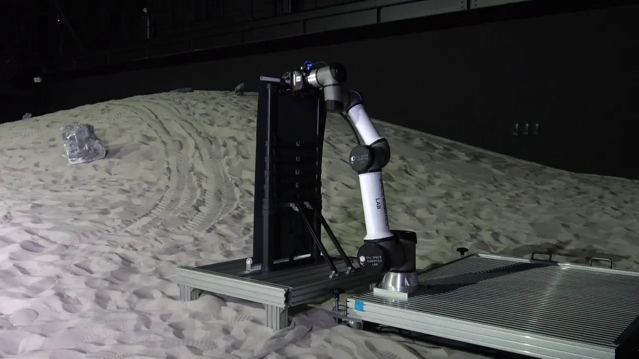 The UR16e arm on its construction pallet, gripping the stowed solar panel stack before extension, JAXA Space Exploration Test Field.