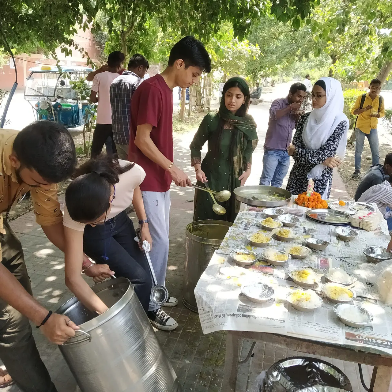 Volunteers serving freshly cooked food into rows of plates at a roadside table.